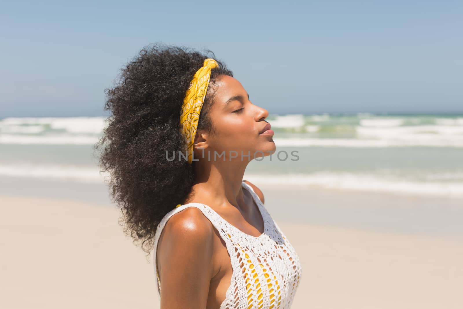 Side view of young African American woman with eyes closed standing on the beach in the sunshine