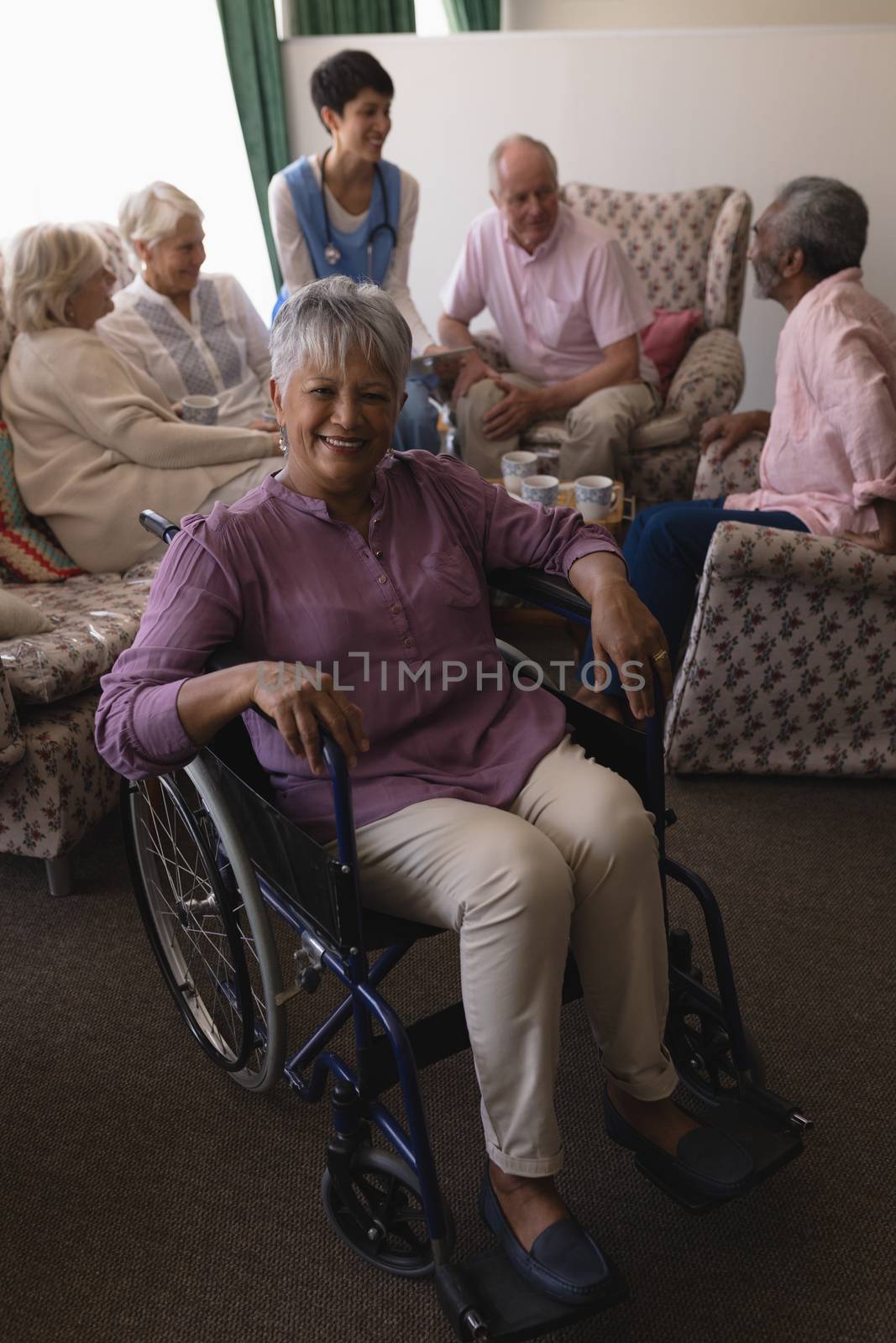 Front view of disabled senior woman smiling with her happy friends behind in living room at home