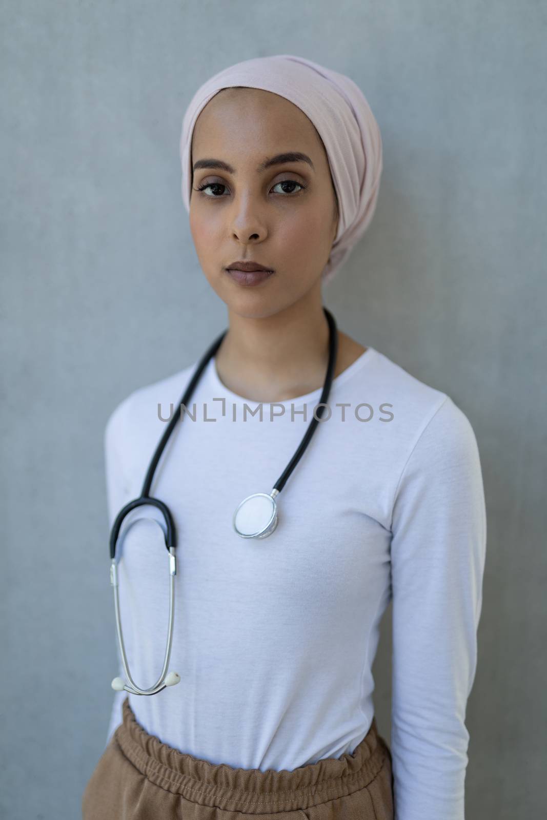 Portrait of beautiful young mixed-race female doctor standing with stethoscope in hospital. She is looking at camera