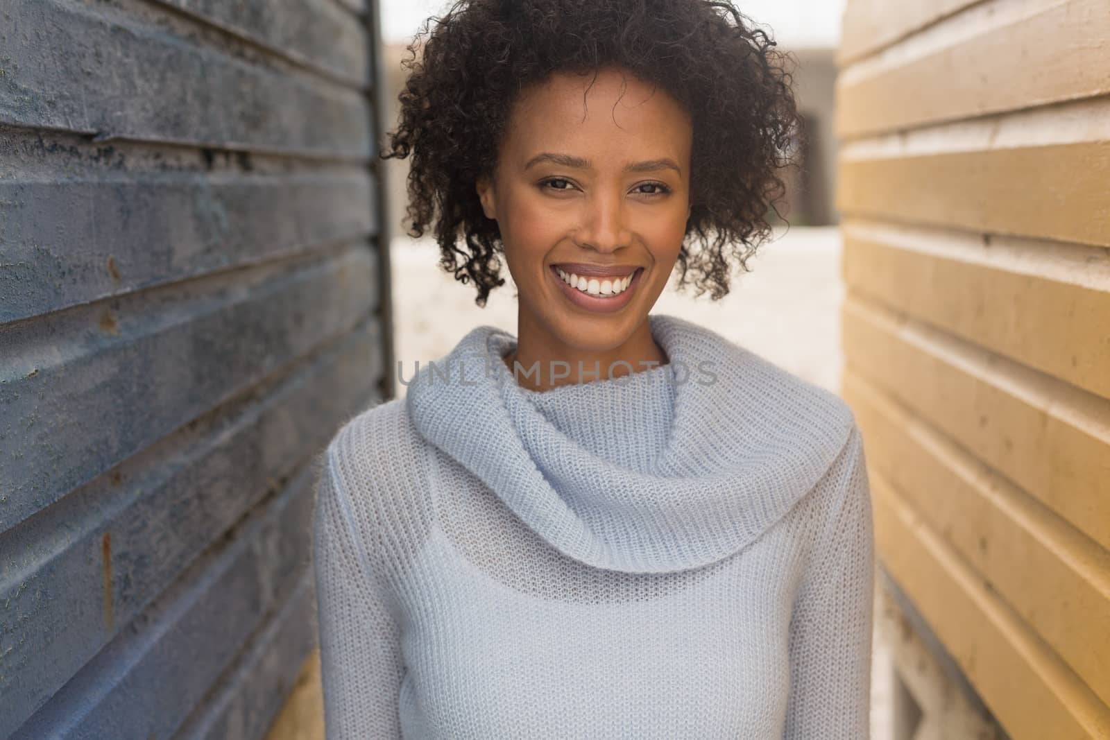 Portrait of happy young African American woman standing at beach hut. She is smiling and looking at camera