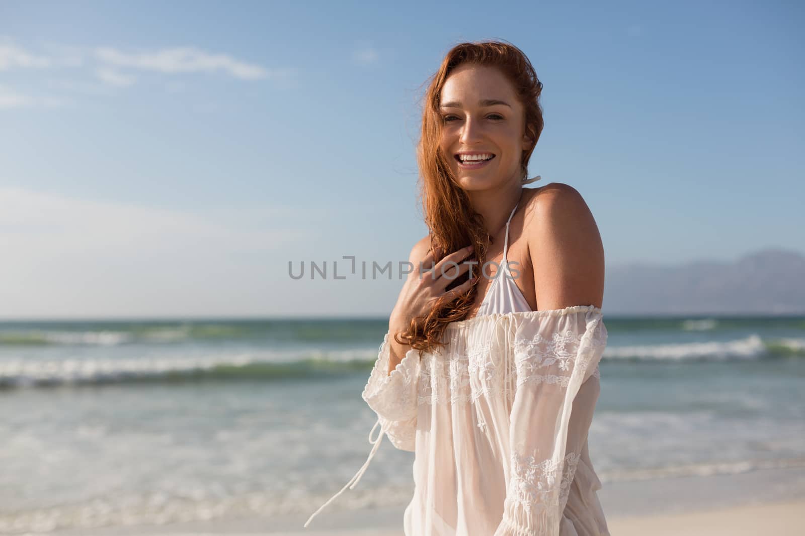 Front view of beautiful happy young Caucasian woman looking at camera standing on the beach. She is smiling