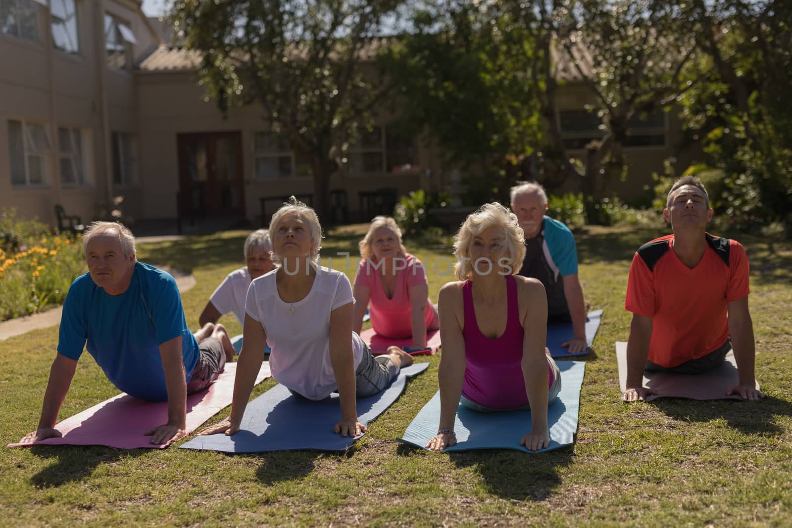 Front view of trainer training senior people in performing exercise on yoga matat park