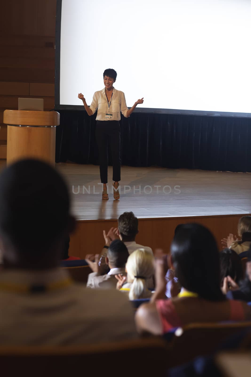 Businesswoman standing and giving presentation in front of the audience in auditorium  by Wavebreakmedia