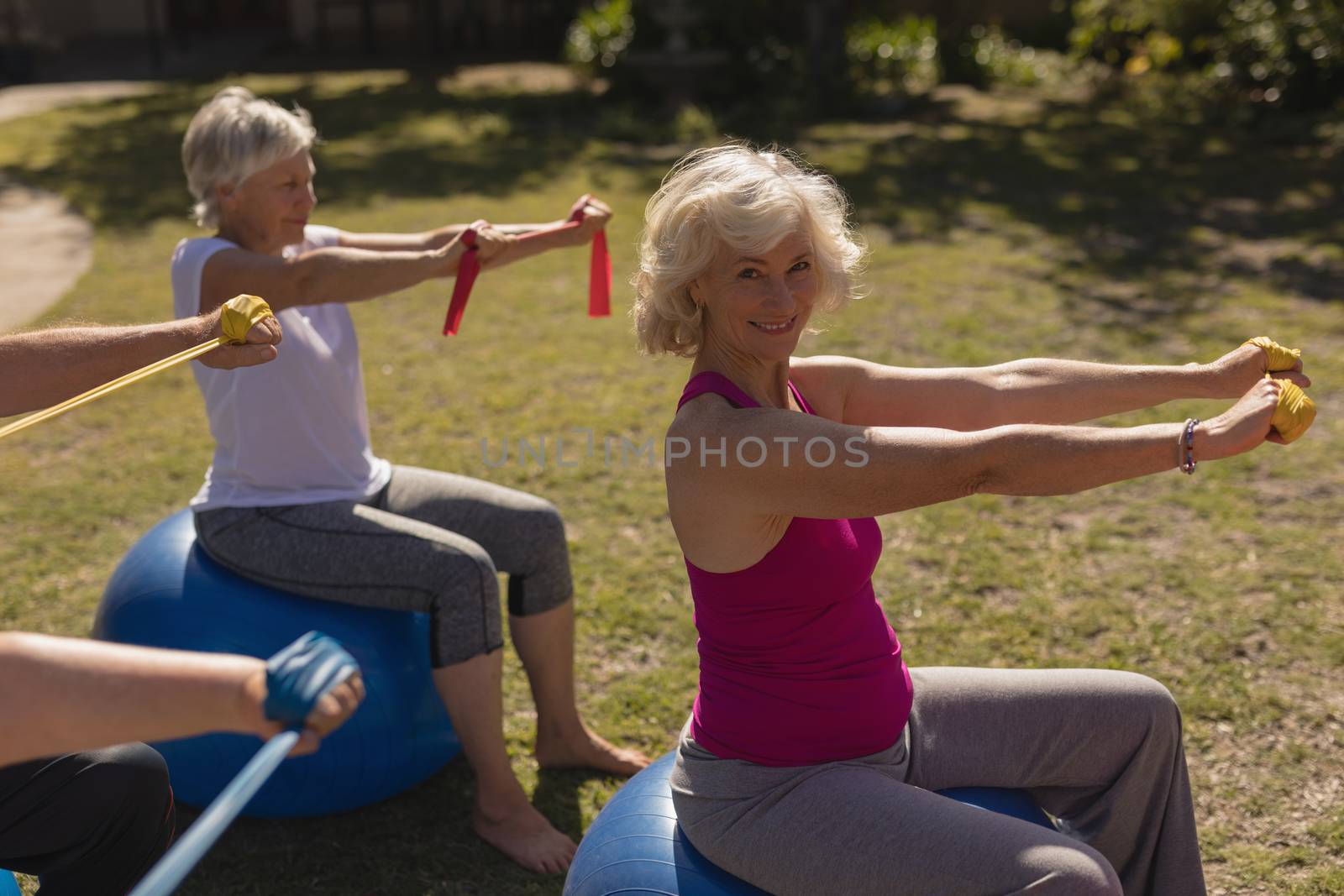 Side view of group of active senior people exercising with elastic band and ball in the park. Senior woman looking the camera 