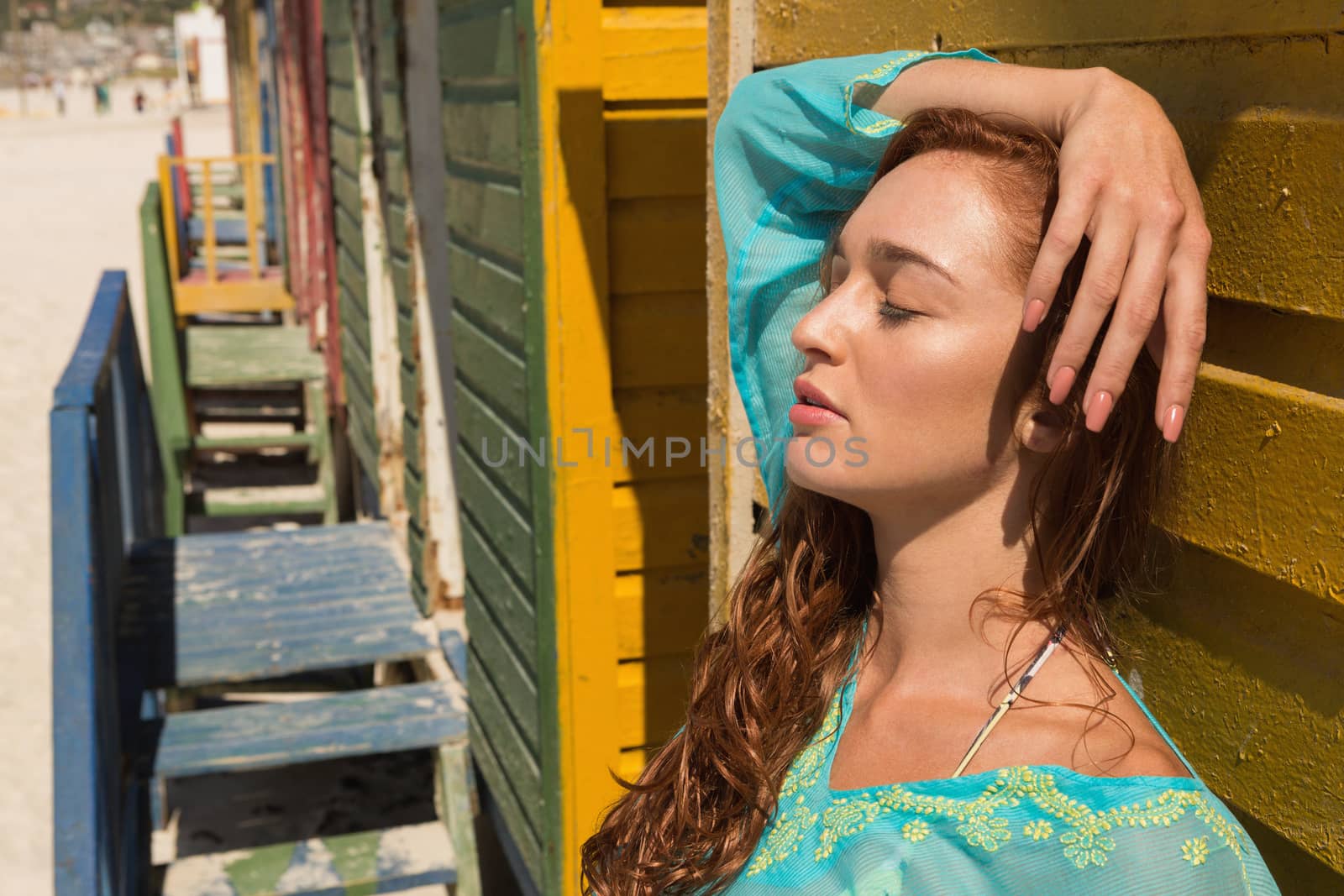 Side view of gorgeous young Caucasian woman with eyes leaning standing against beach hut at beach. She seems relaxex