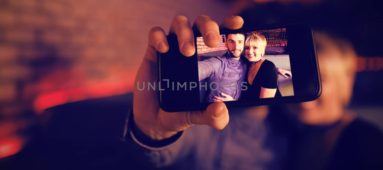 Smiling couple taking selfie on mobile phone in bar