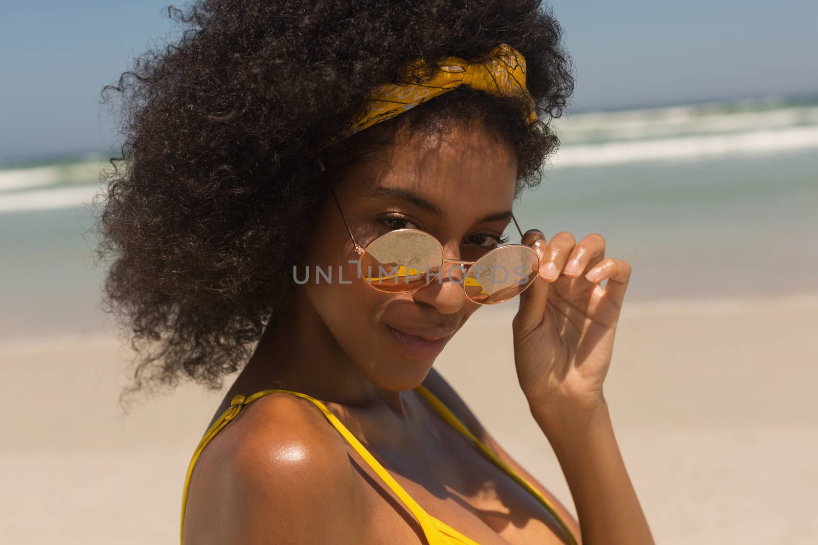 Portrait of young African American woman in bikini looking over sunglasses on the beach