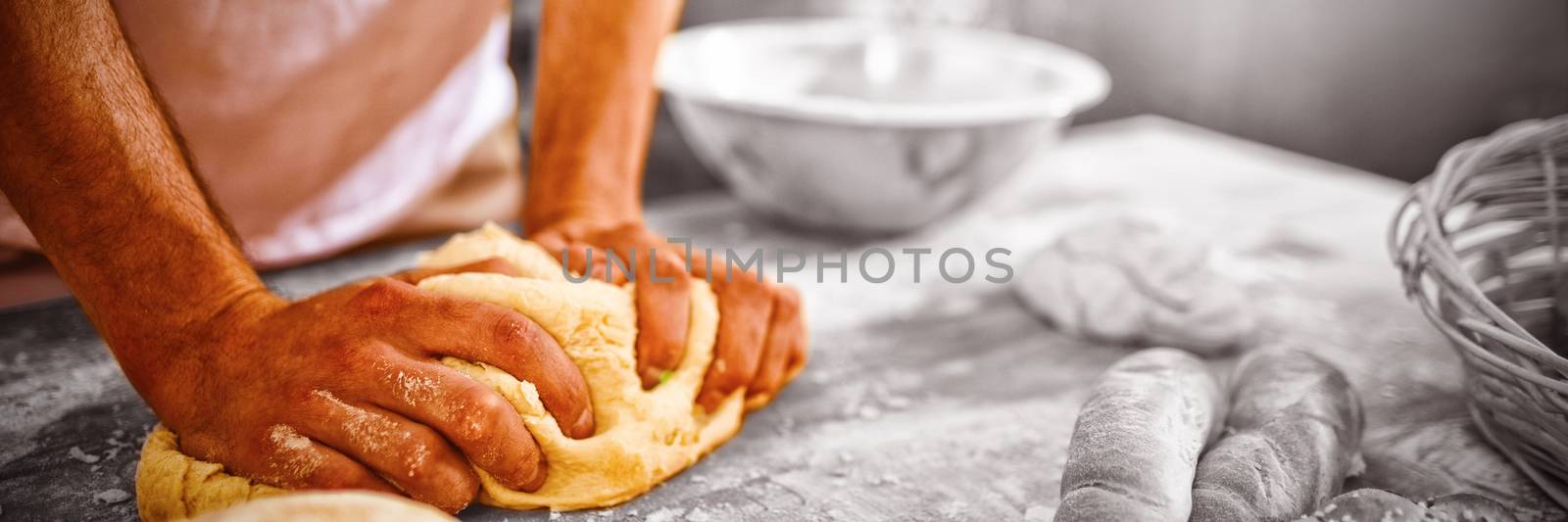 Mid section of baker kneading dough in bakery shop