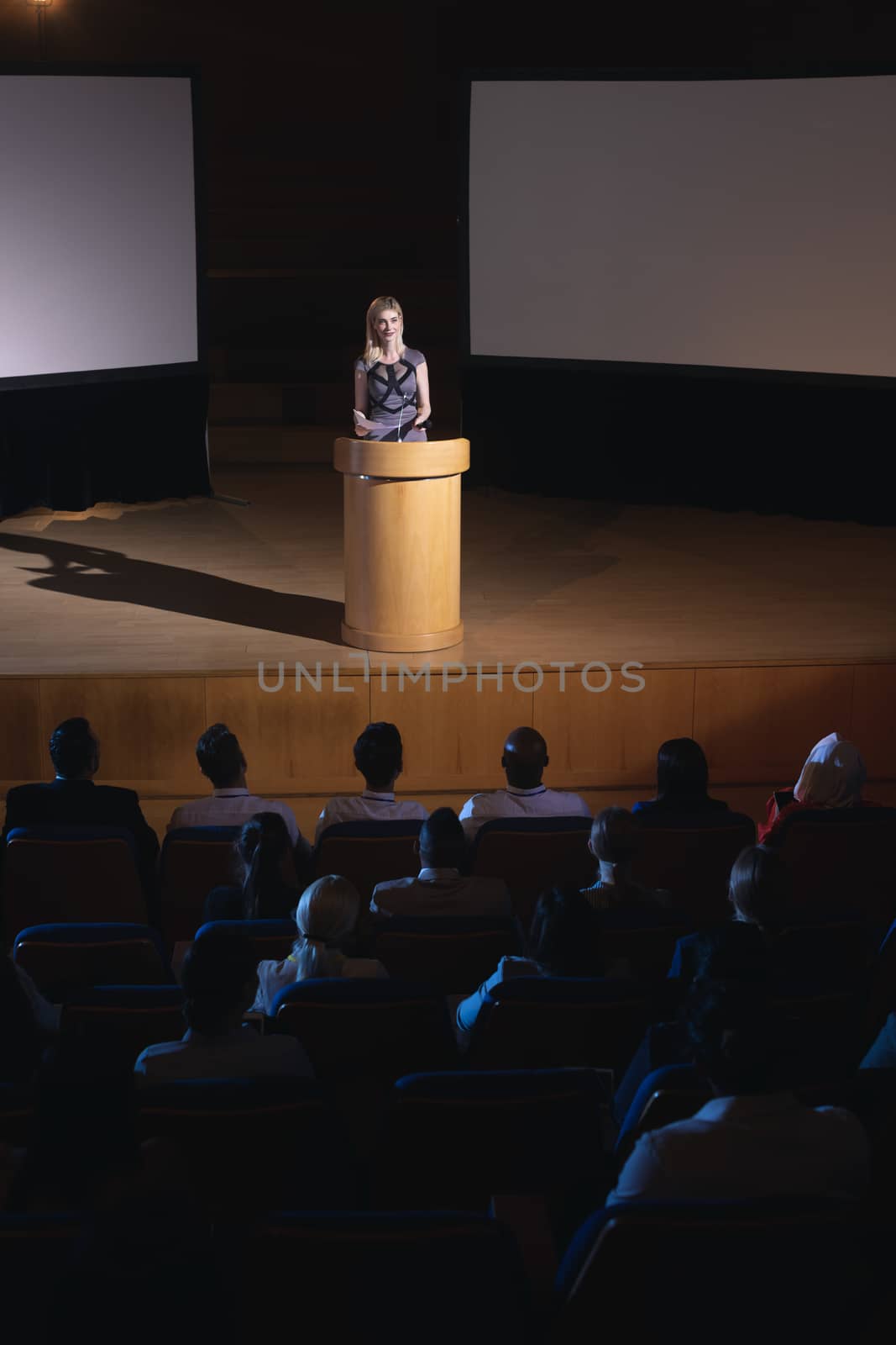 High view of blonde Caucasian businesswoman standing around podium and giving presentation to the audience in auditorium