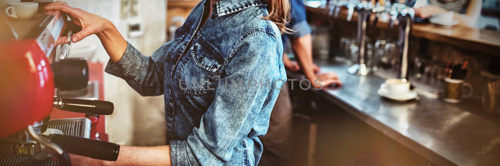 Portrait of happy waitress with co-worker talking to young female customer at coffee shop