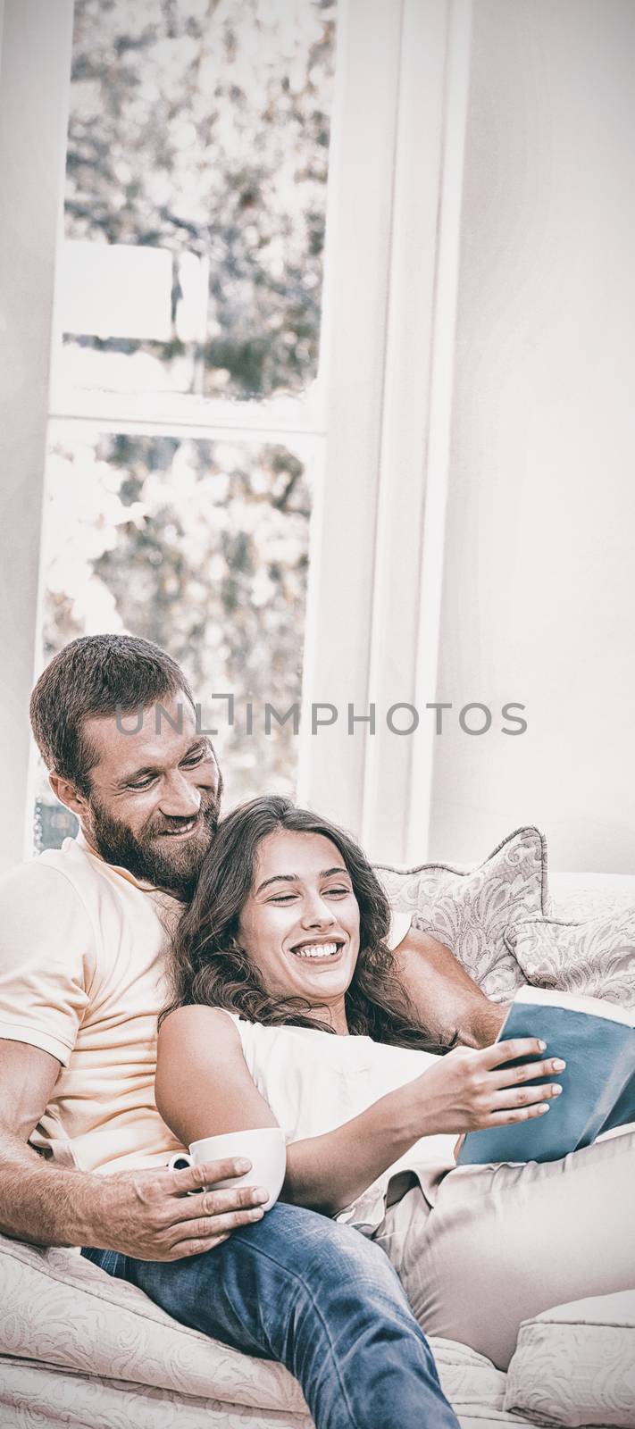 Man holding a cup of coffee while woman reading book by Wavebreakmedia