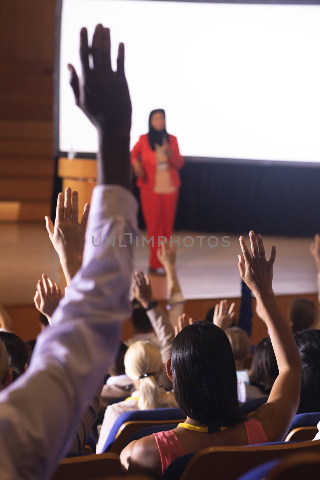 Rear view of mixed race audience raising hand for asking question in the auditorium