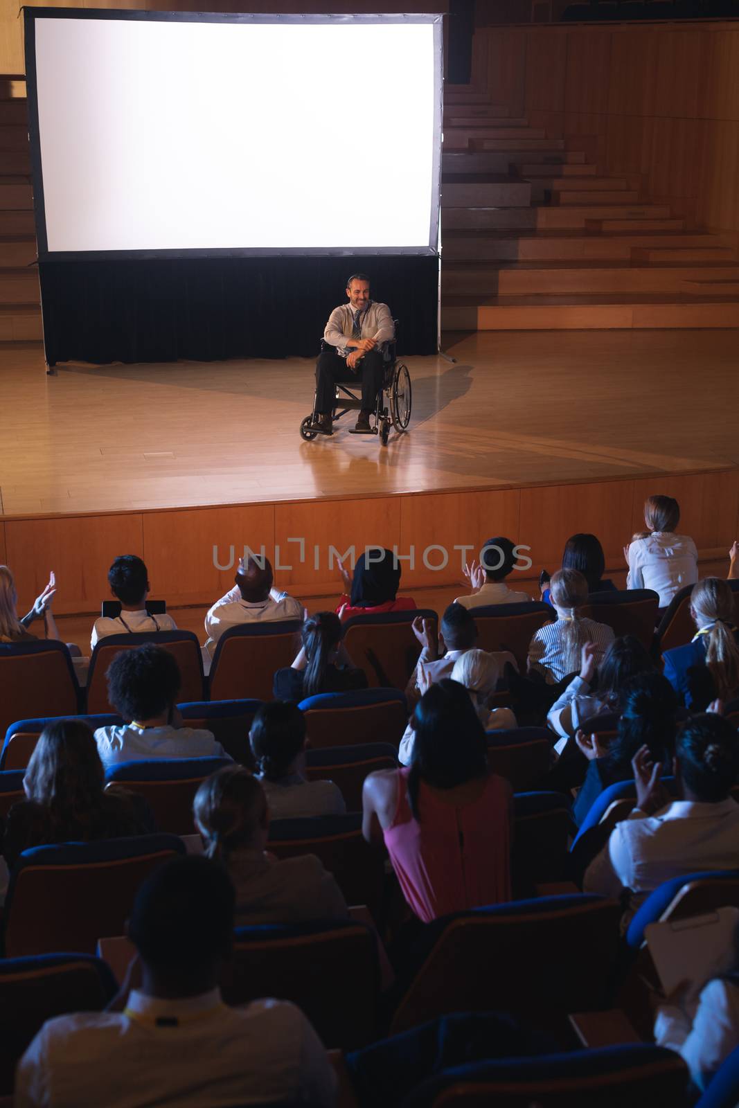 High view of Caucasian businessman sitting on a wheelchair and giving presentation to the audience in the auditorium