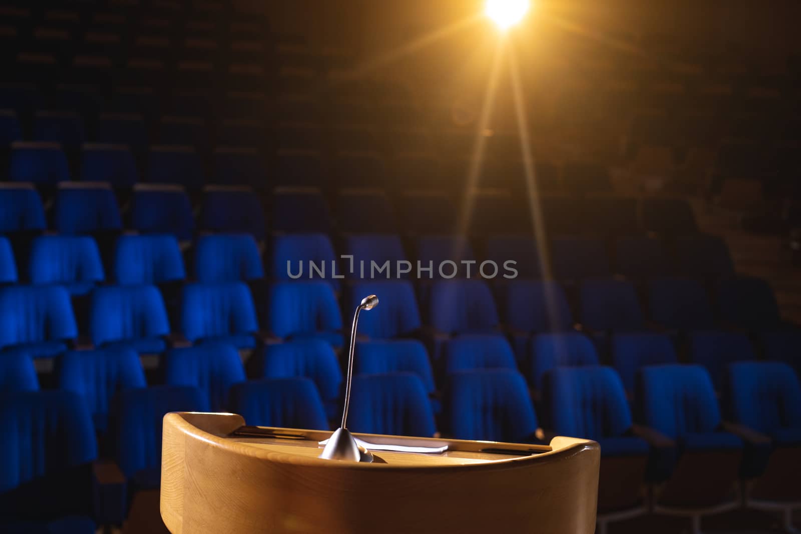 Front view of empty auditorium with podium and speaker on stage with orange light in the background