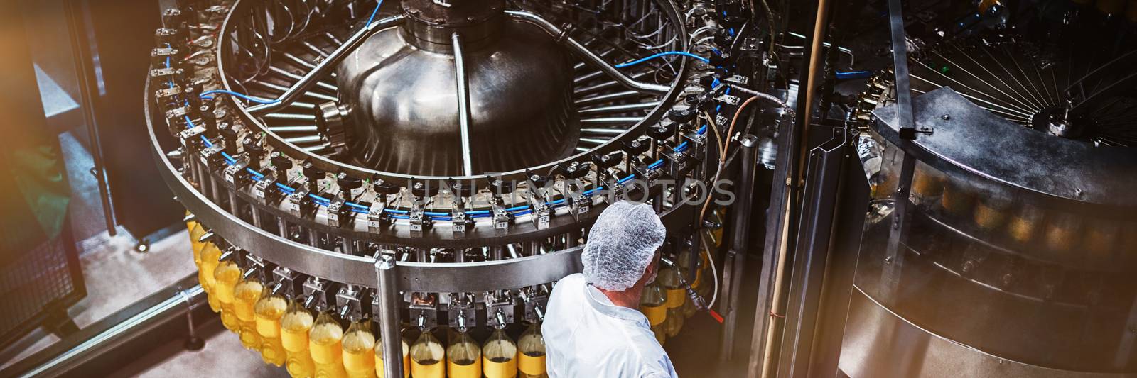 Factory engineer monitoring filled juice bottle on production line in bottle factory