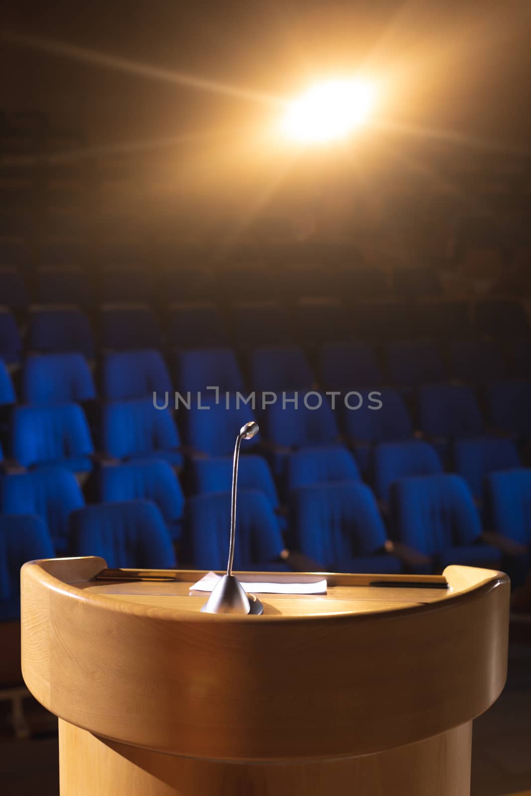 Front view of empty auditorium with podium and speaker on stage with orange light in the background