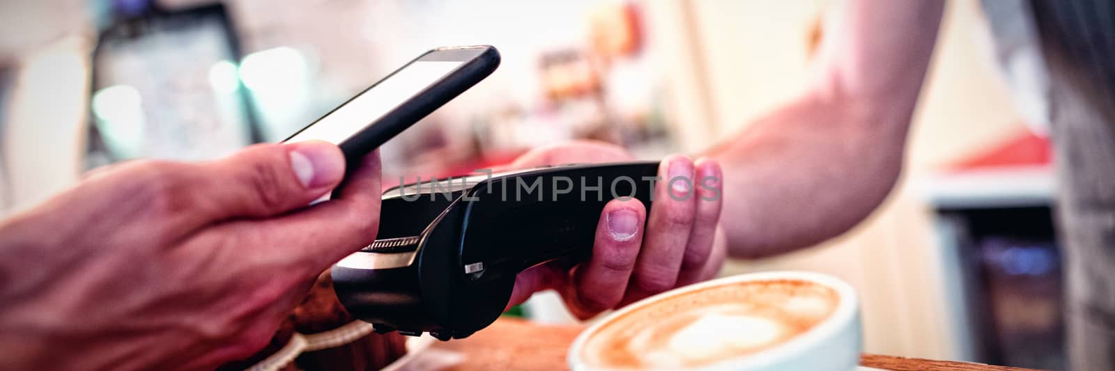 Close-up of customer with cellphone and barista with card reader by Wavebreakmedia