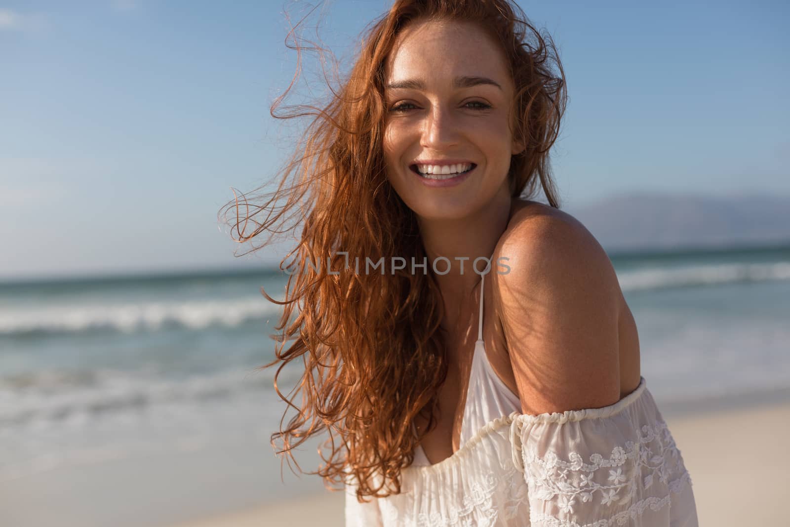Front view of beautiful happy young Caucasian woman looking at camera standing on the beach. She is smiling