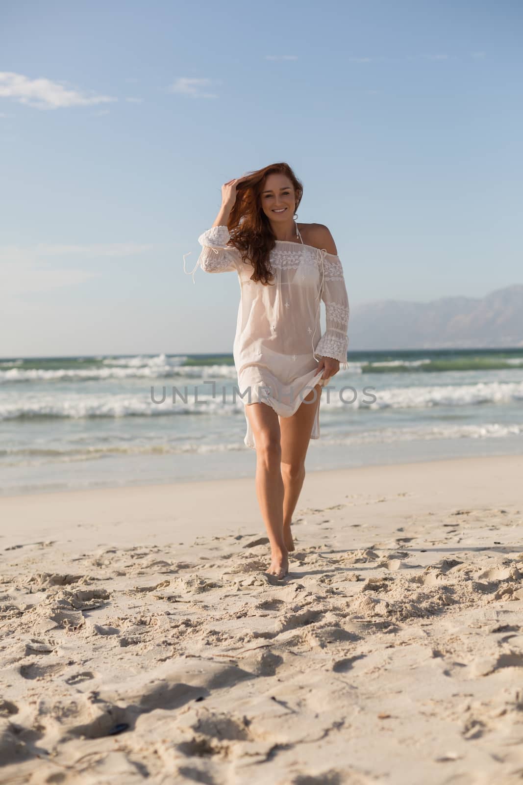 Portrait of beautiful young Caucasian woman walking on the beach in the sunshine. She is smiling