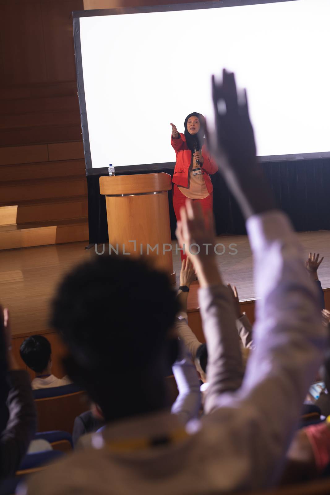 Front view of mixed race businesswoman listening and asking while audience raising hand for the queries in the auditorium