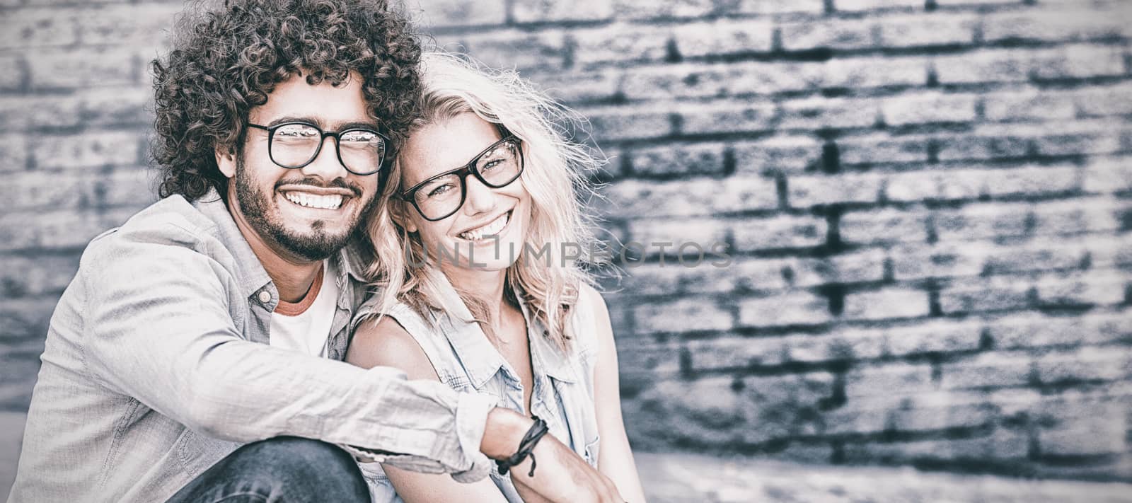 Portrait of happy young couple in spectacles sitting on footpath