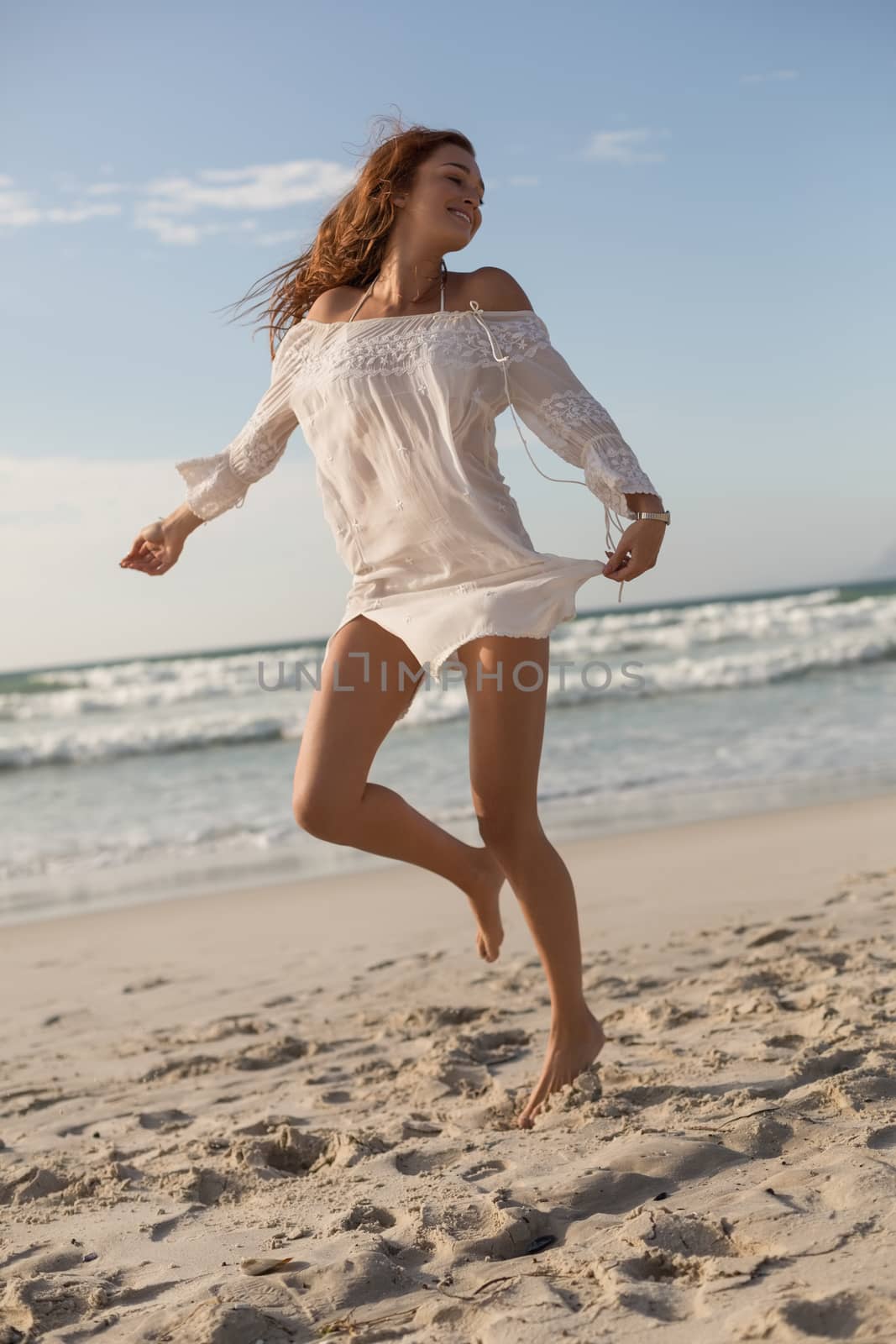 Front view of happy beautiful young Caucasian woman dancing on the beach. She seems happy