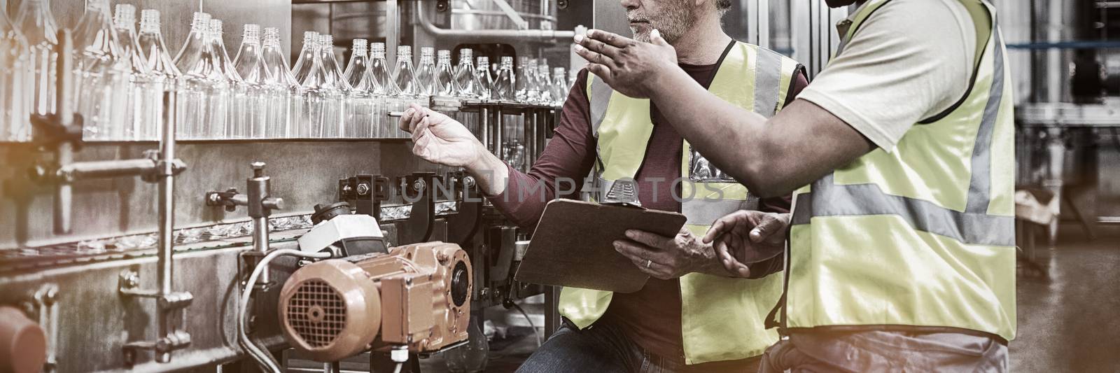 Two factory workers discussing while monitoring drinks production line by Wavebreakmedia