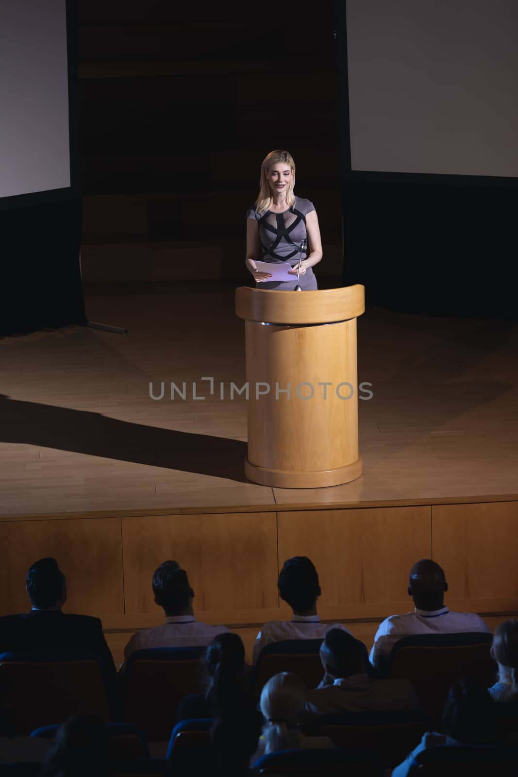 Hight view of blonde Caucasian businesswoman standing around podium and giving presentation to the audience in auditorium