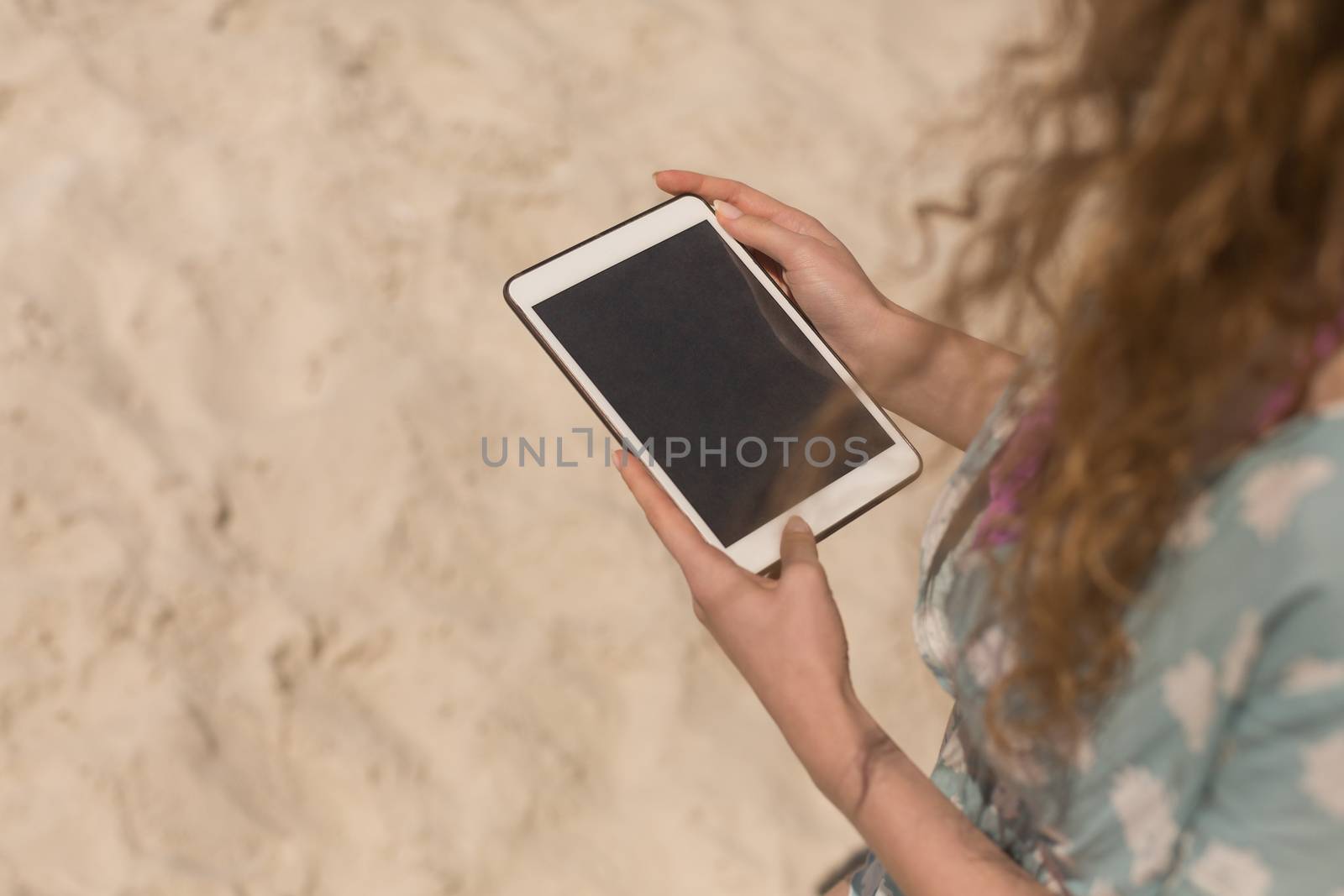 Midsection of young Caucasian woman using digital table on beach. It is sunny day