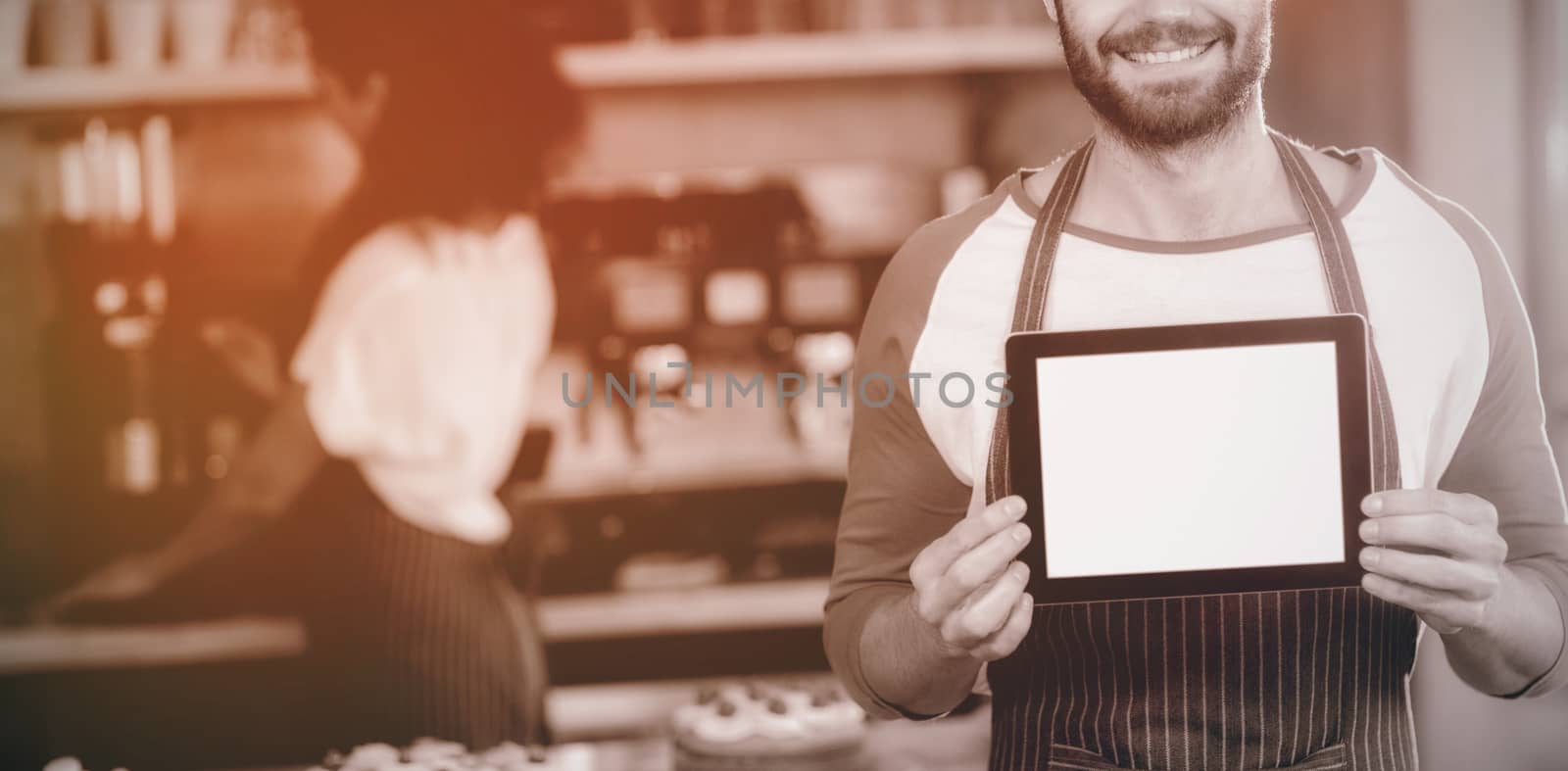 Portrait of smiling waiter showing digital tablet at counter in cafÃ©