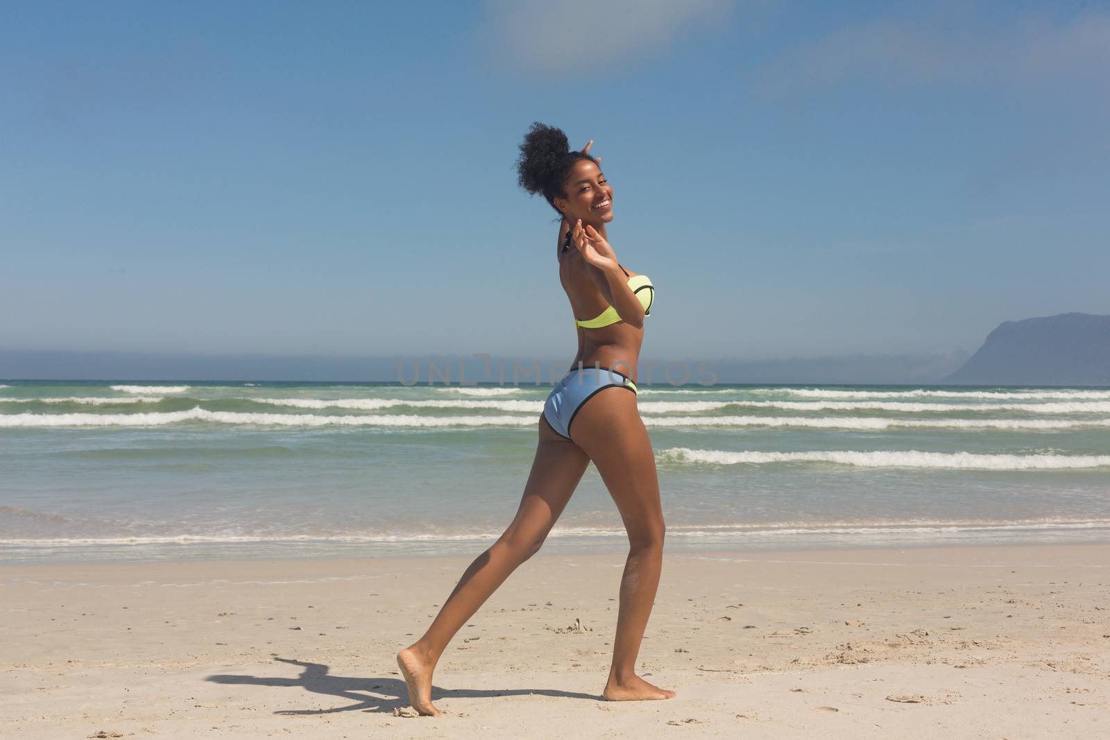 Portrait of pretty happy young African American woman in green bikini playing on the beach. She is smiling and looking at camera