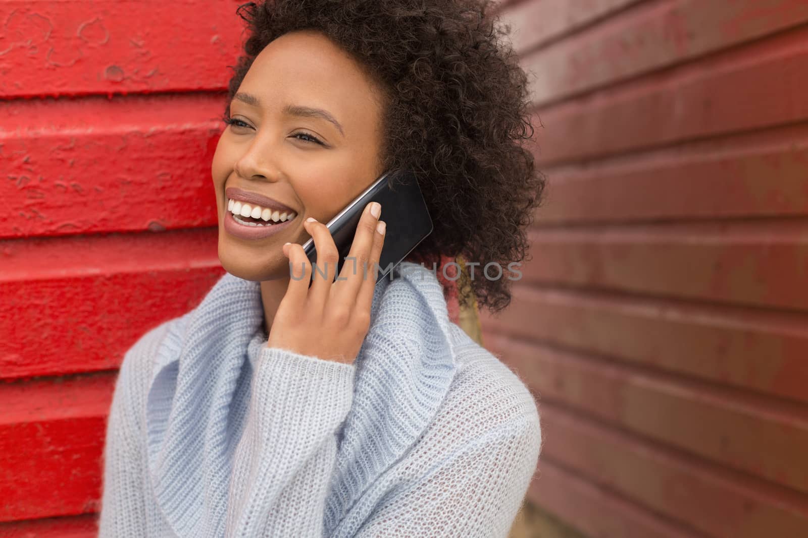 Front view of pretty happy young African American woman talking to her mobile phone at red beach hut. She is smiling