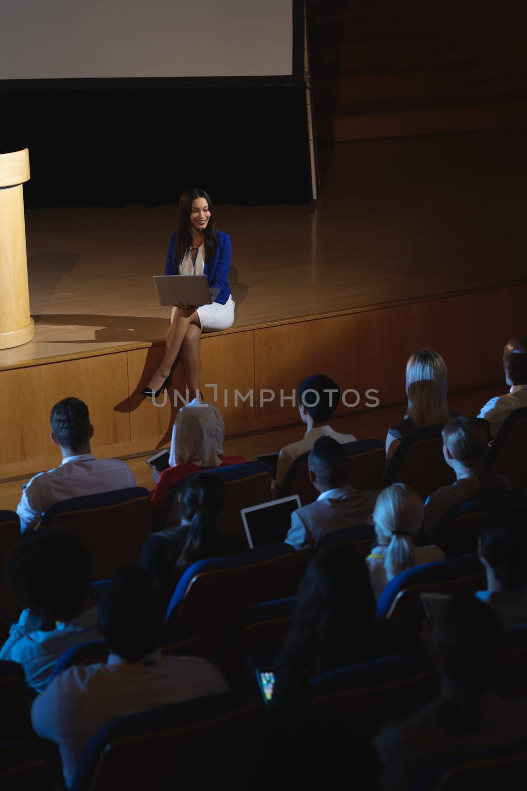 Businesswoman sitting at the side of the stage and having laptop in her hand  by Wavebreakmedia