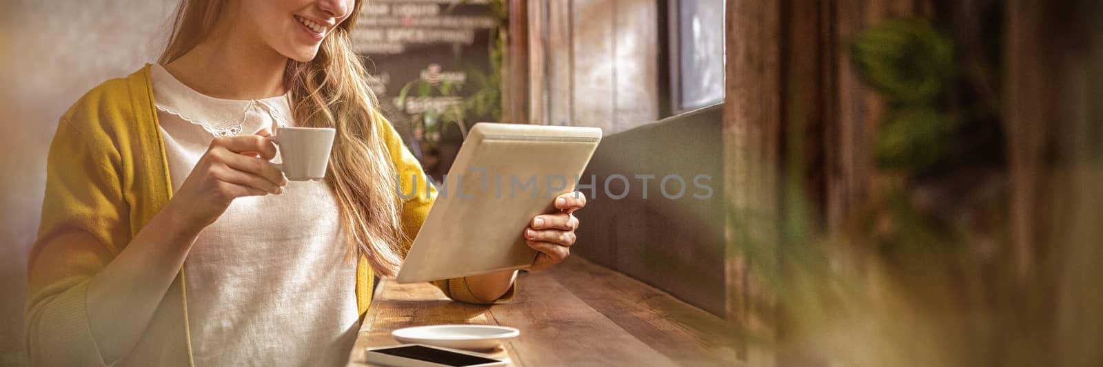 Smiling woman drinking coffee and using tablet by Wavebreakmedia