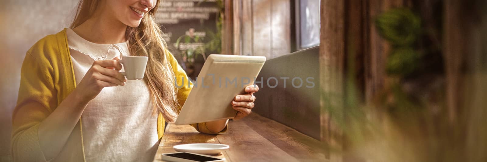 Smiling woman drinking coffee and using tablet in the cafe