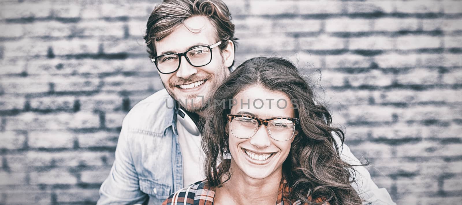 Portrait of happy young couple in spectacles sitting against brick wall