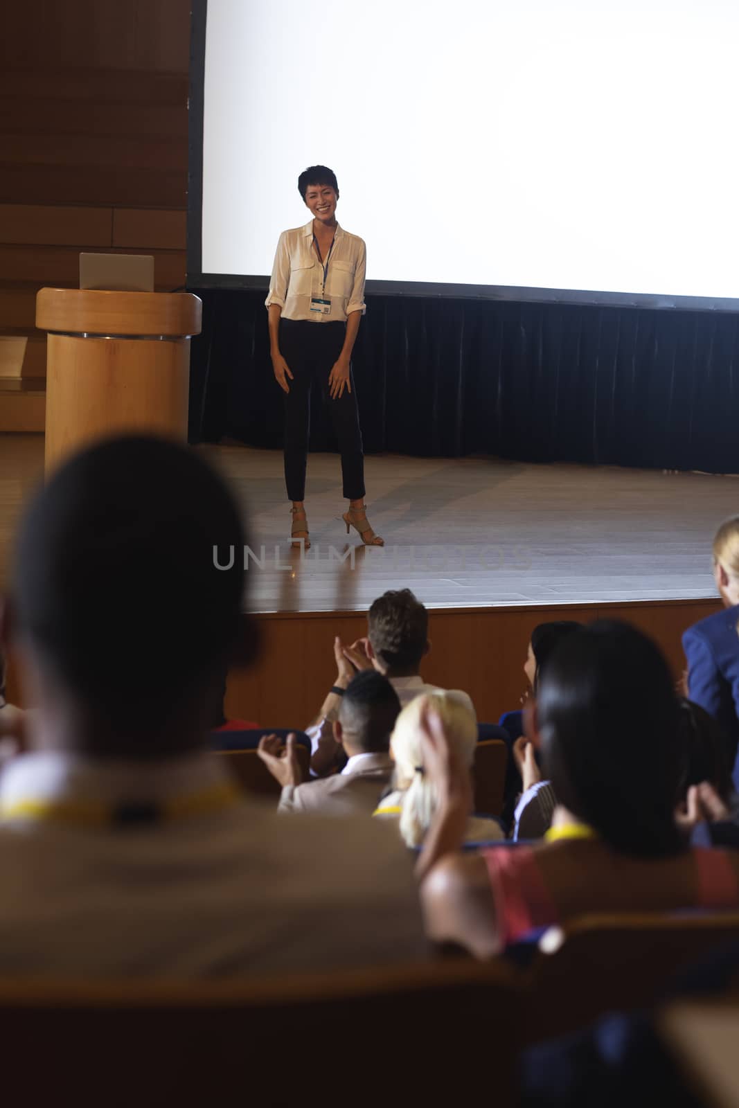 Businesswoman standing and giving presentation in front of the audience in auditorium  by Wavebreakmedia