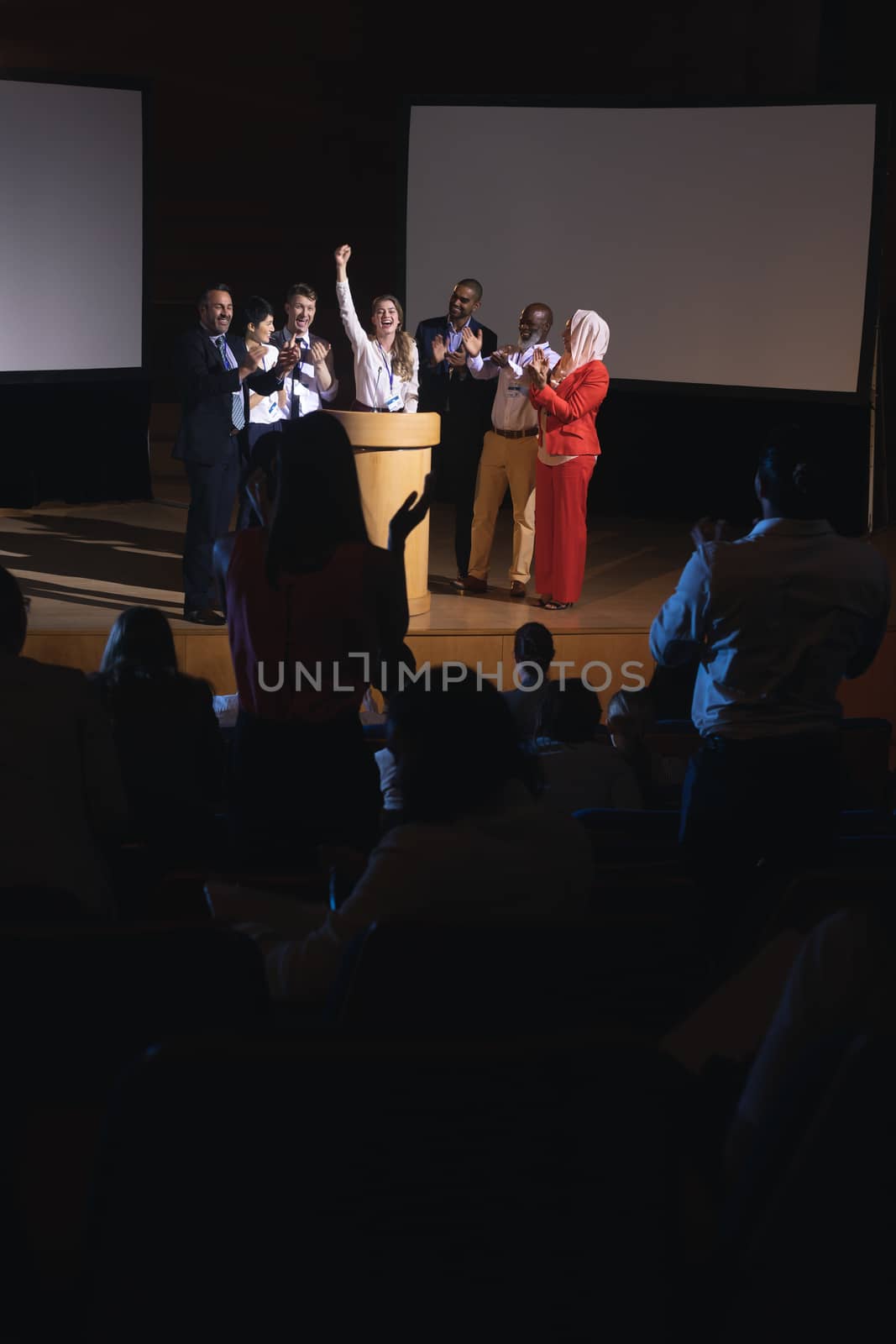 High view of happy Caucasian businesswoman standing at the stage of the auditorium with colleagues in front of audience