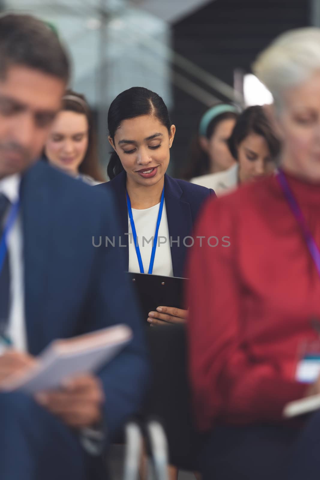 Front view of beautiful young mixed race businesswoman writing on notepad in a business seminar in office building