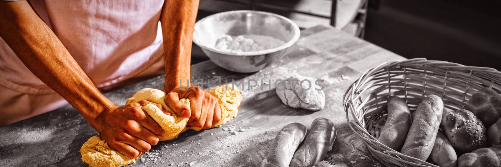 Mid-section of baker kneading a dough in bakery shop