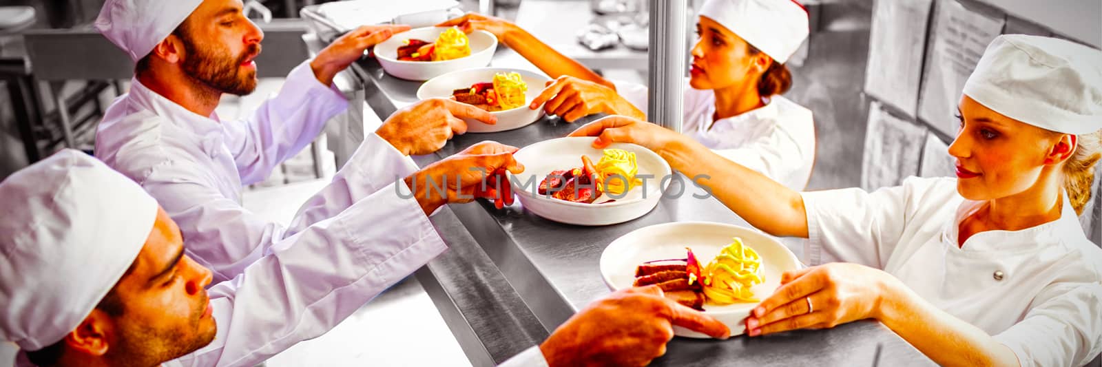 Chefs passing ready food to waiter at order station in commercial kitchen