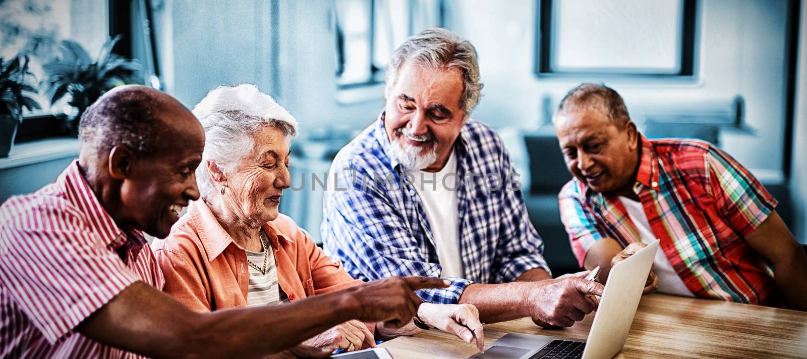 Happy senior men and woman using laptop while sitting at table in nursing home