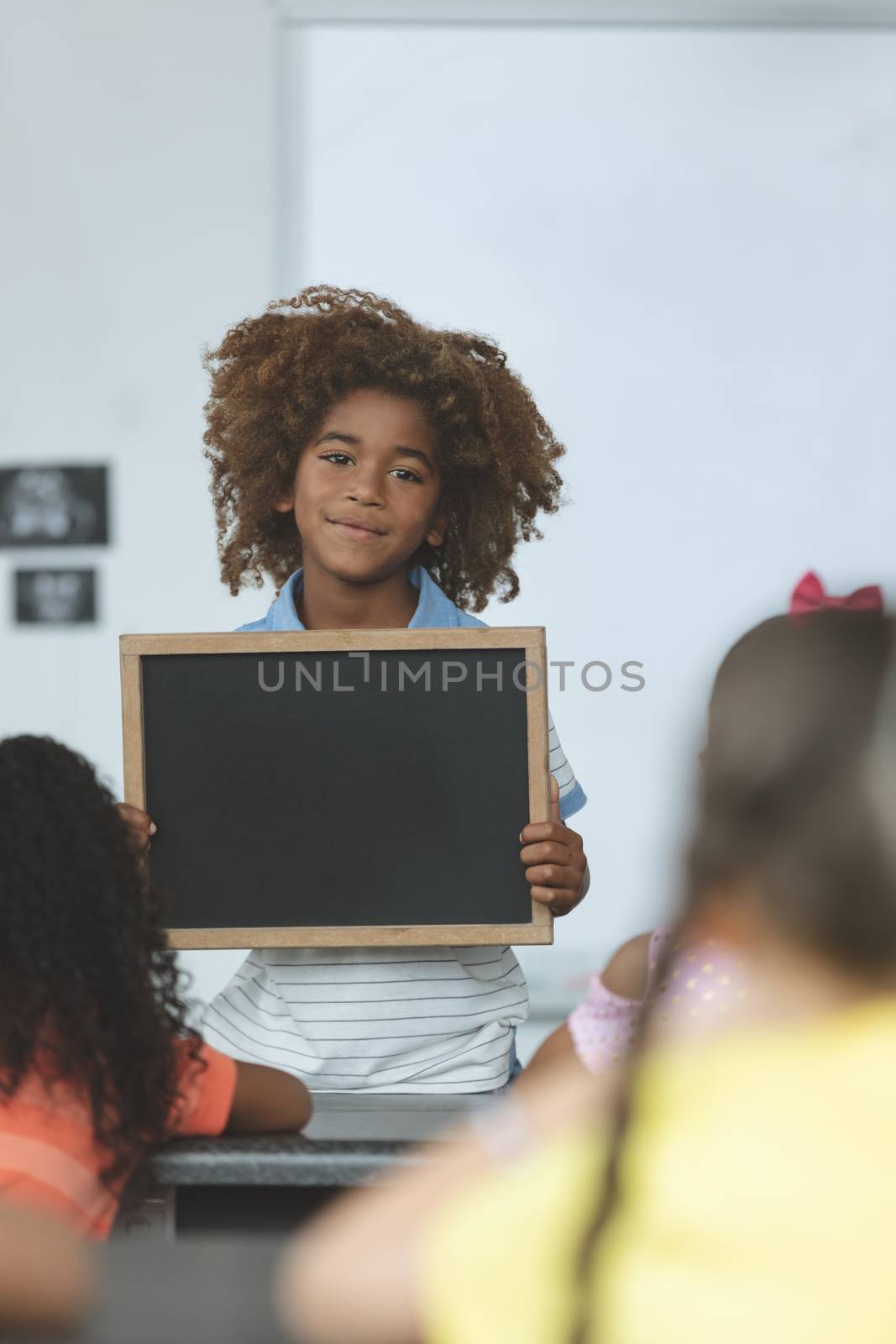 Front view of an Arican ethnicity schoolboy holding a slate and looking at camera in classroom