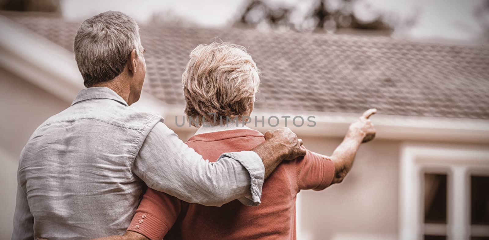 Rear view of senior couple looking at house while standing in yard 