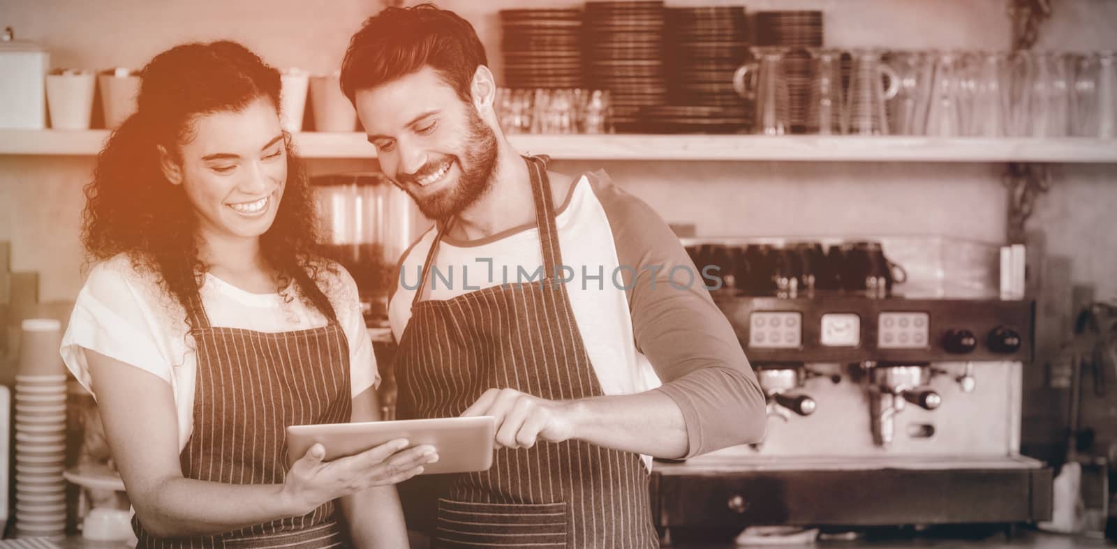 Smiling waiter and waitress using digital tablet at counter in cafe