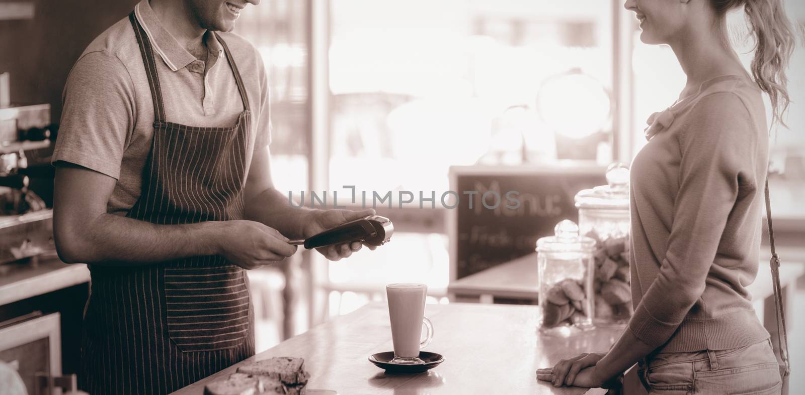 Customer making payment through payment terminal at counter in cafÃ©