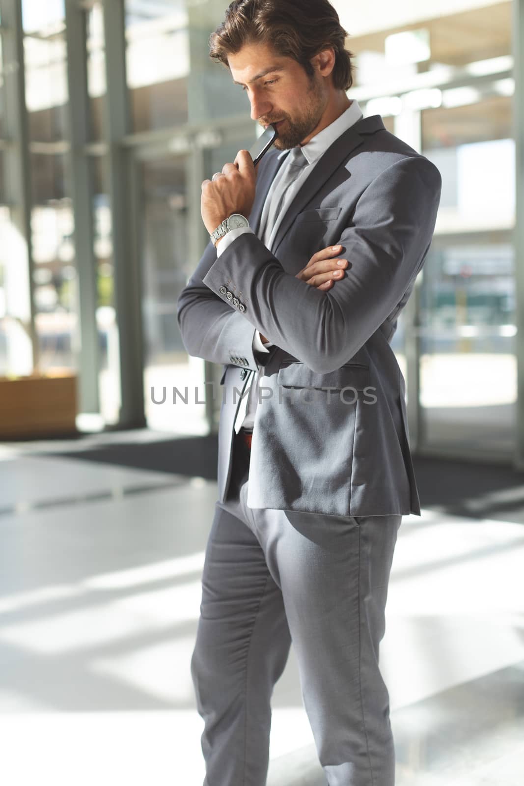 Side view of thoughtful young Caucasian businessman with head down with his mobile phone standing in office