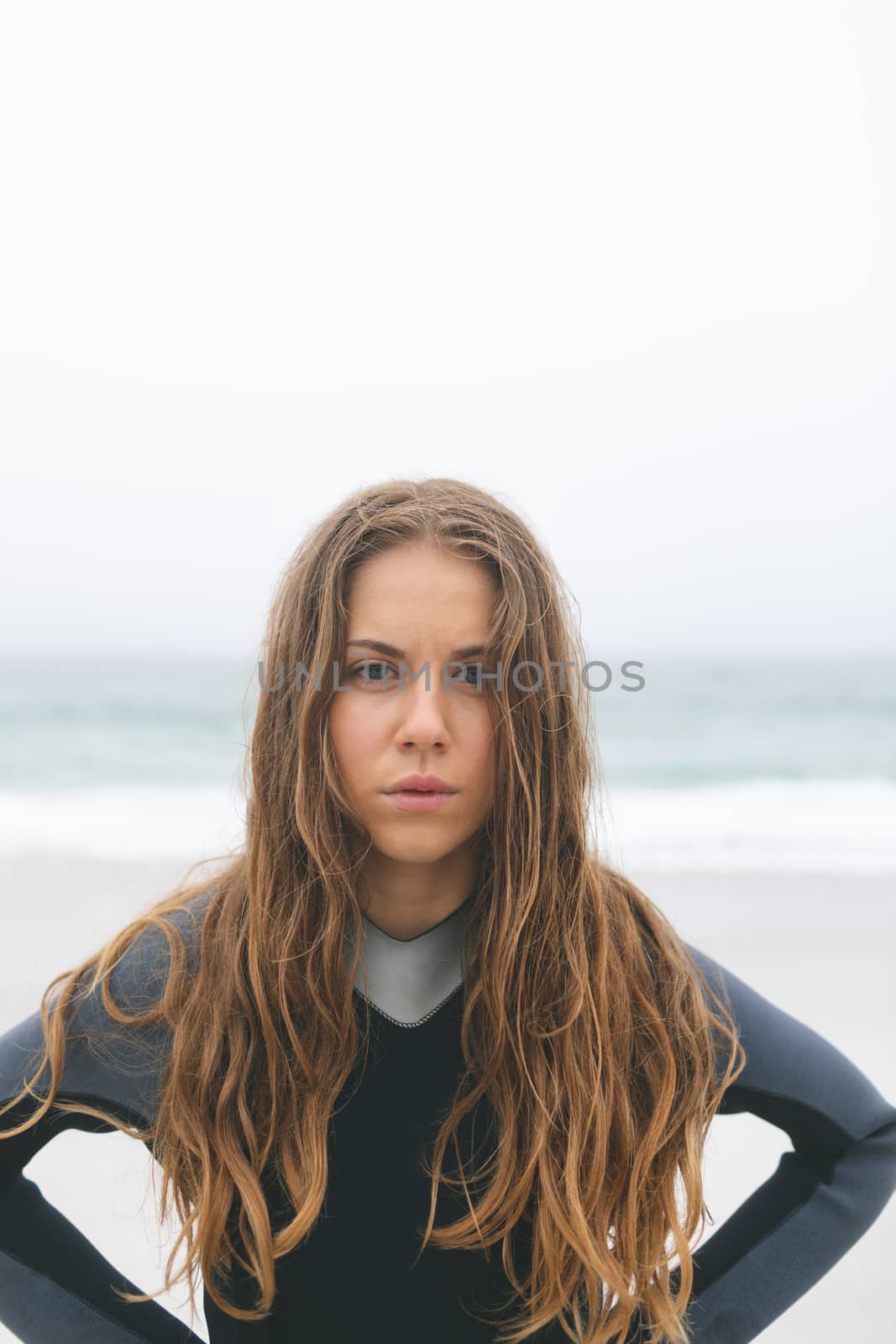 Portrait of woman standing with hands on hips on the beach. She is looking at camera