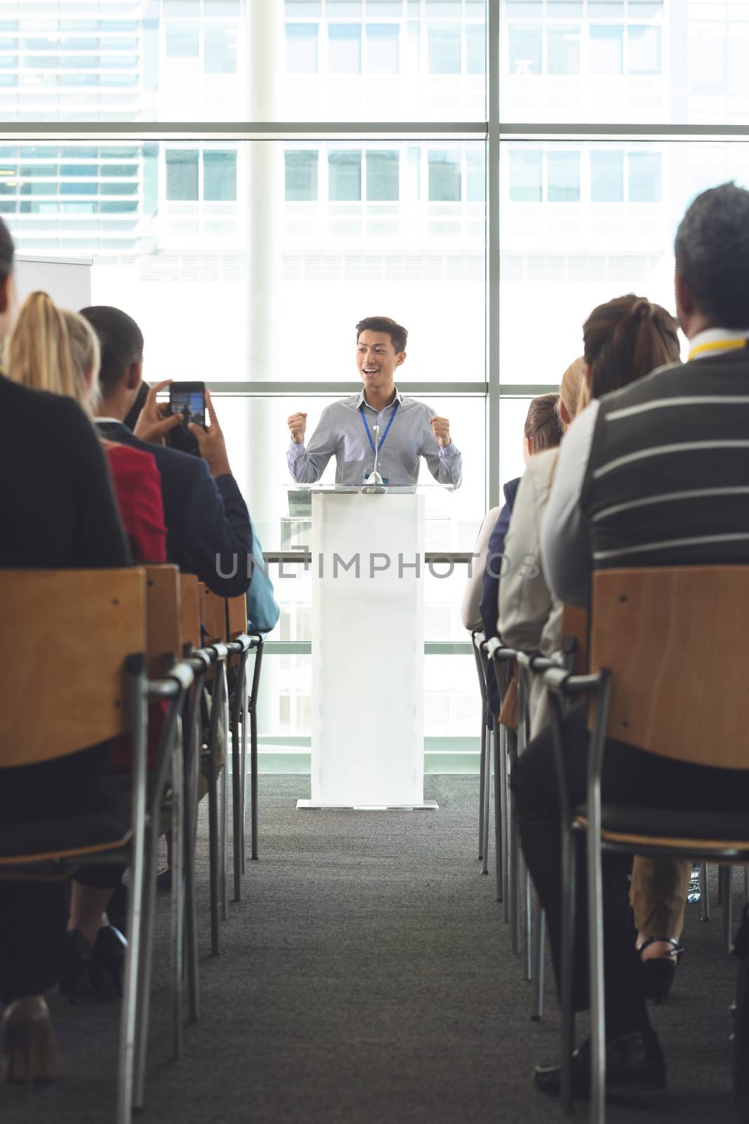 Front view of young Asian businessman speaking while business people sit in front of him at business seminar in office building