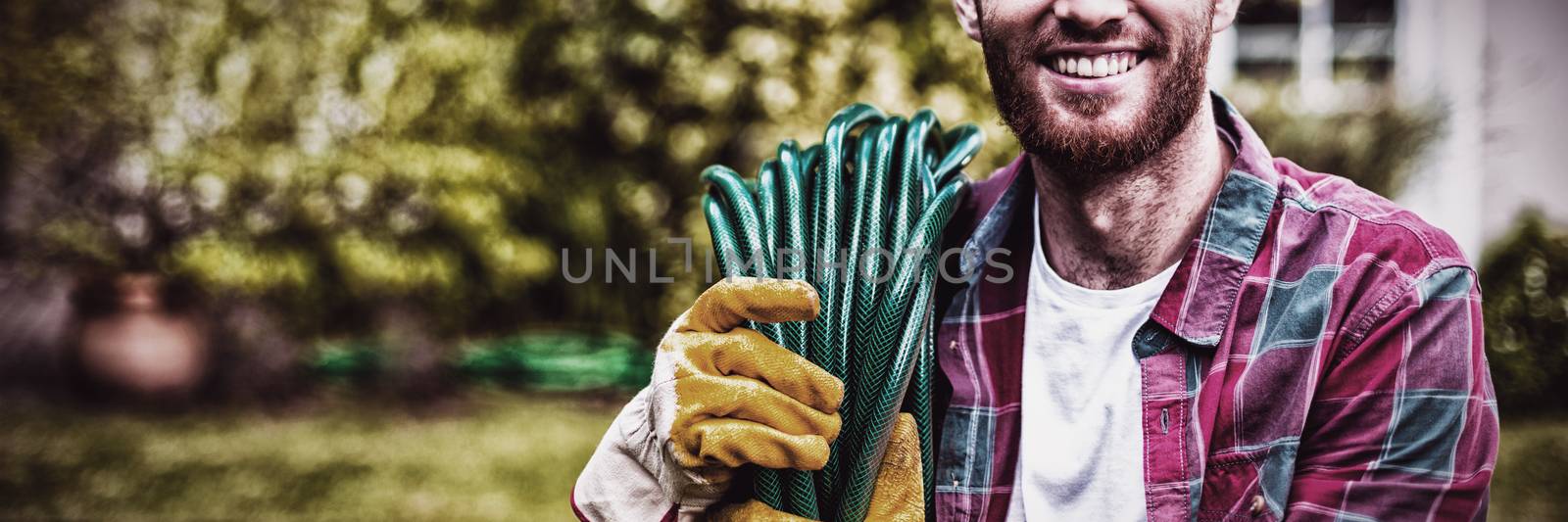 Smiling man carrying garden hose while standing in backyard 